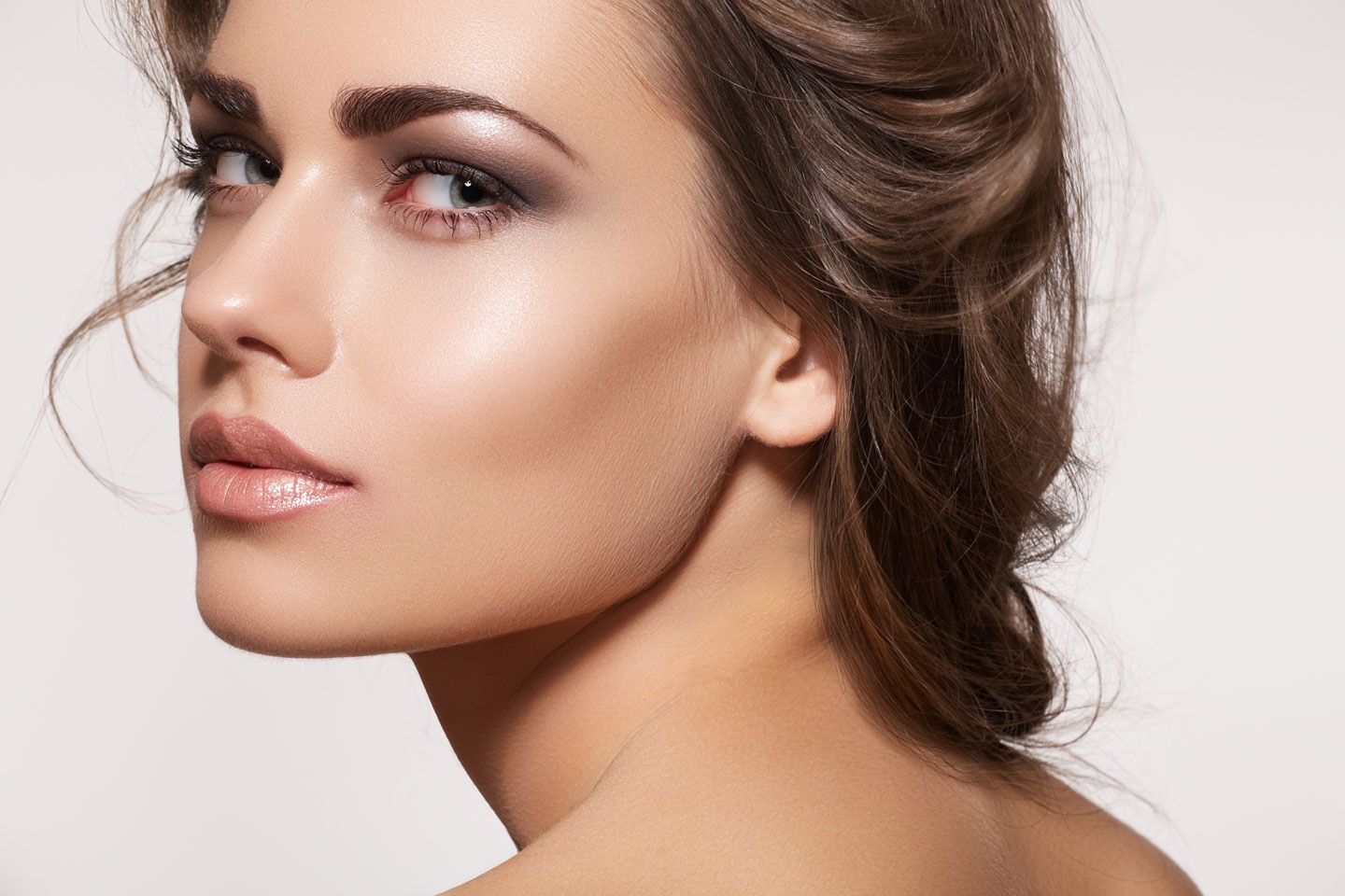 Glamour portrait of beautiful woman model with fresh daily make-up and romantic wavy hairstyle. Fashion shiny highlighter on skin.